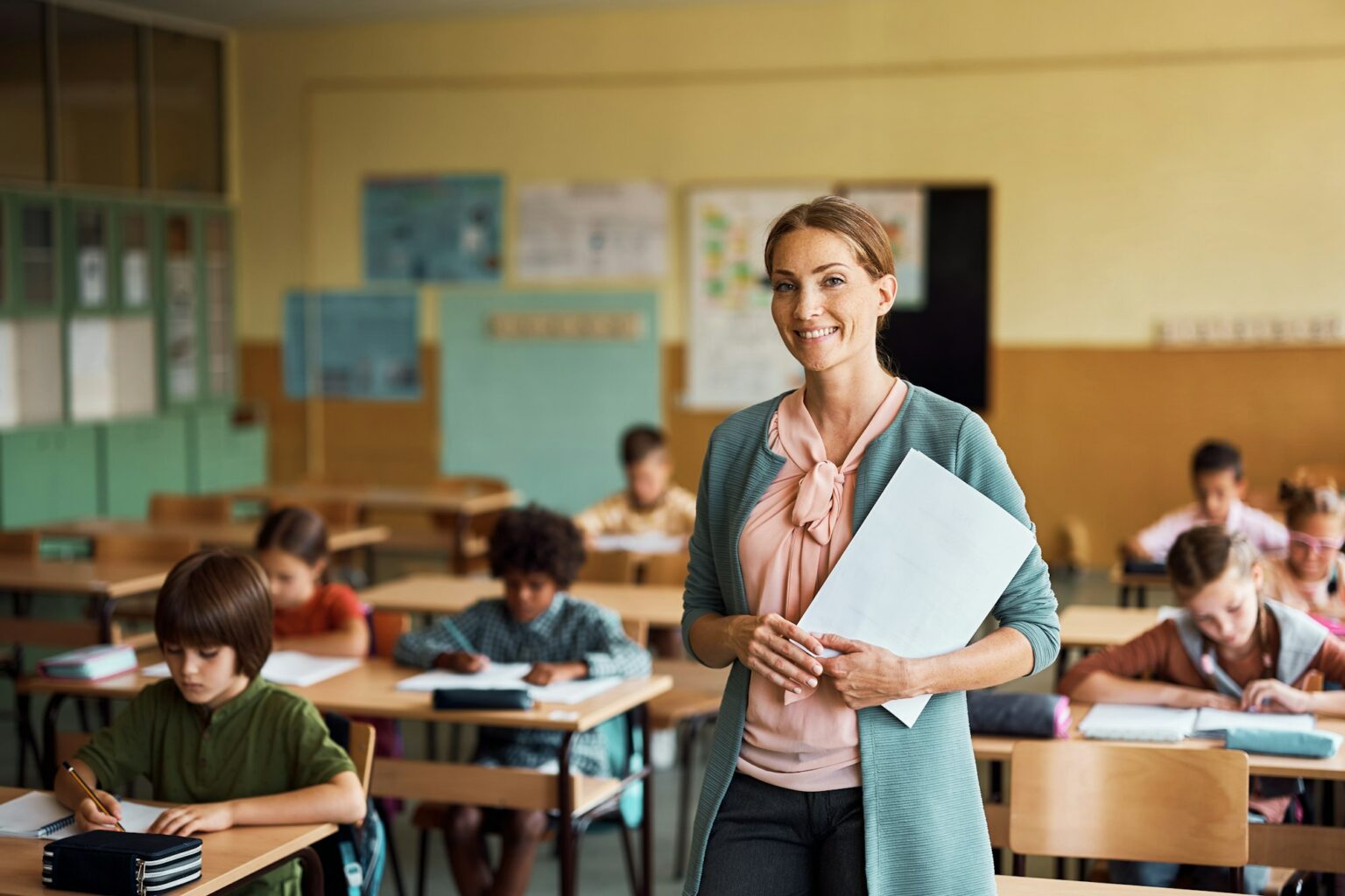 Happy elementary school teacher in the classroom looking at camera.