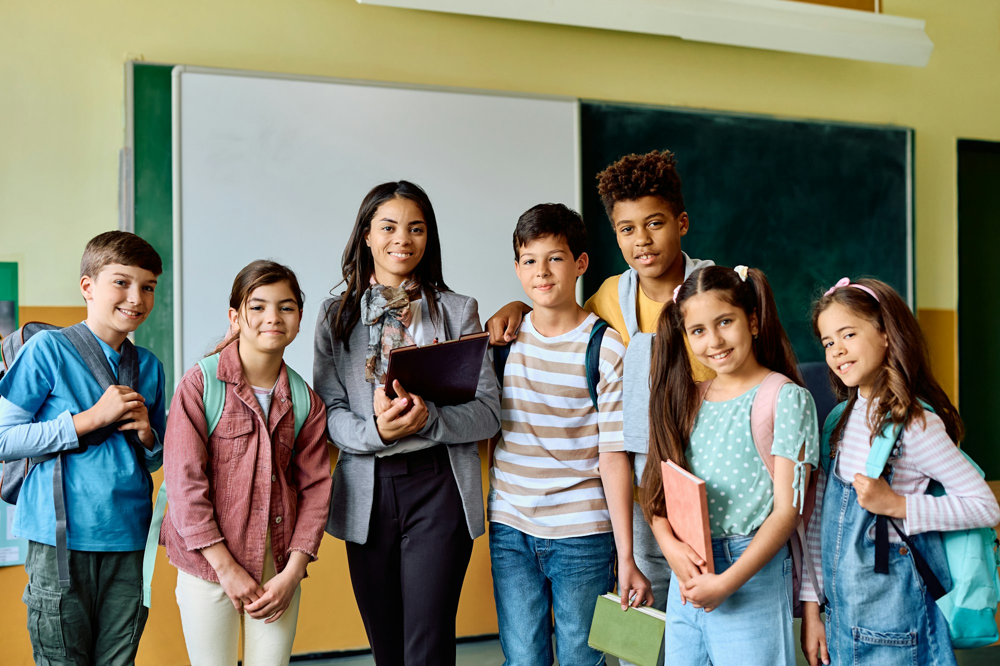 Multiracial group of school kids with their teacher in the classroom looking at camera.